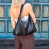 Mała czarna torebka na ramię LUNA w miękkim fasonie slouchy hobo, prezentowana na modelce.